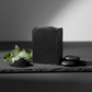 Handcrafted matte black activated charcoal soap bar on slate surface with eucalyptus sprig and charcoal powder